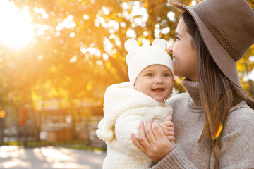 Happy mother with her baby daughter outdoors on autumn day, space for text