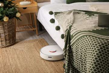 Modern robot vacuum cleaner near bed in room - obrazy, fototapety, plakaty