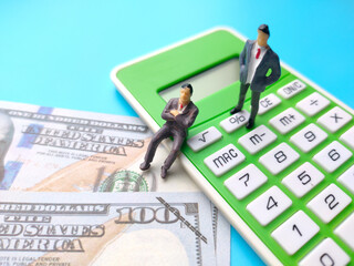Miniature people,banknotes and calculator on a blue background. Business concept idea.