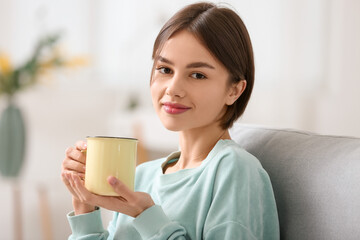 Beautiful young woman drinking tasty tea on sofa at home