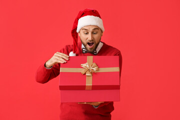 Surprised young man opening Christmas gift on color background