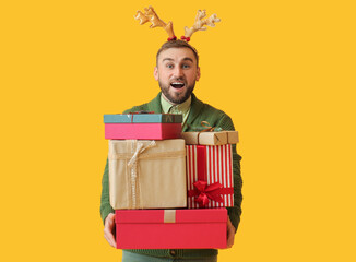 Surprised young man with Christmas gifts on color background
