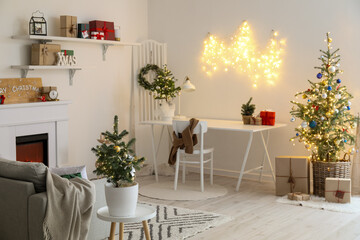 Interior of light living room with modern workplace, Christmas trees and glowing lights