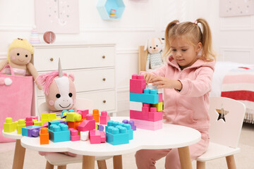 Fototapeta na wymiar Cute little girl playing with colorful building blocks at table in room