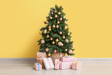 Beautiful Christmas tree with pink gift boxes near yellow wall