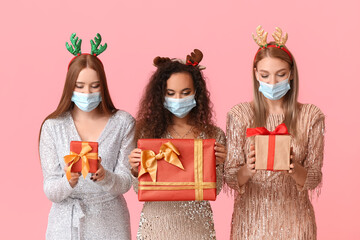 Beautiful young women in medical masks and with Christmas gifts on color background