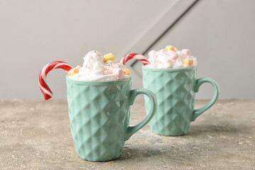 Cups of tasty cacao with marshmallows and candy cane on grey background