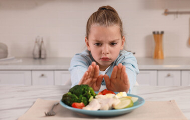 Cute little girl refusing to eat dinner in kitchen