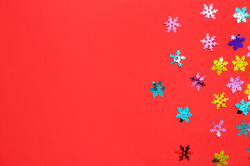 Colorful confetti in shape of snowflakes on red background