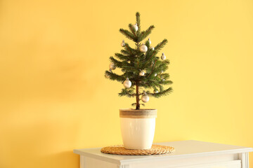 Beautiful decorated Christmas tree in pot on table near yellow wall