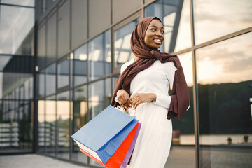 Arabic woman wearing hijab standing with shopping bags near mall