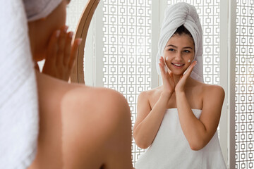Beautiful teenage girl applying cleansing foam onto face near mirror at home. Skin care cosmetic