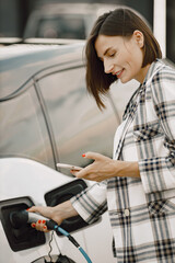 Businesswoman on the electric cars charge station using a phone