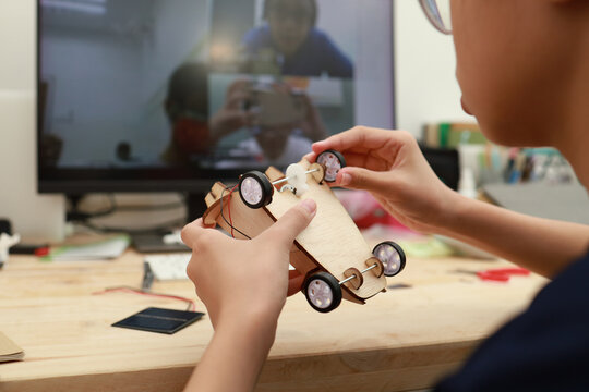 Teenage Asian girl building a solar toy car through online e-learning at home. Student doing school project or learning science through video call with teacher. Soft focus image.