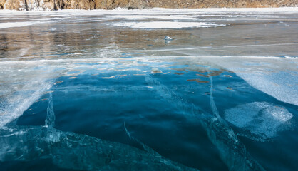 Blue transparent ice of a frozen lake. Close-up. Cracks extending into the depths are visible, a little snow on the surface. Baikal