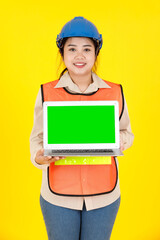Portrait studio shot of Asian female professional engineering foreman manager in hard helmet and reflect safety vest hold blank green screen laptop computer for text copy space on yellow background