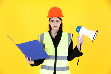 Portrait studio shot Asian female professional engineering foreman with braces in hard helmet and reflect safety vest smiling look at camera holding megaphone and document folder on yellow background