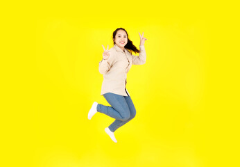 Fototapeta na wymiar Portrait studio shot of Asian young happy female chubby plump model in casual outfit long sleeve shirt and denim jeans pants smiling look at camera jumping high exercise alone on yellow background