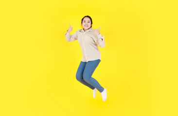 Fototapeta na wymiar Portrait studio shot of Asian young happy female chubby plump model in casual outfit long sleeve shirt and denim jeans pants smiling look at camera jumping high exercise alone on yellow background