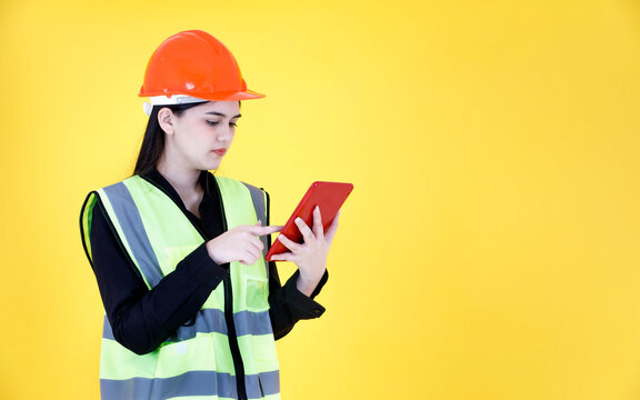 Studio Shot Asian Female Professional Engineering Foreman Manager With Braces In Hard Helmet And Reflective Safety Vest Smiling Greeting Say Hi Hello Goodbye On Tablet Video Call On Yellow Background