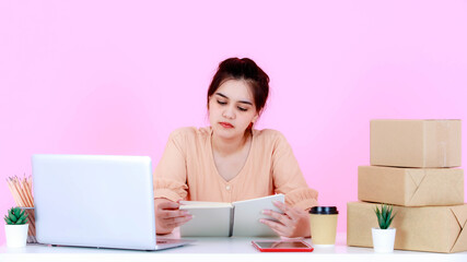 Studio shot of Asian happy successful professional young female startup entrepreneur businesswoman working at table on pink background