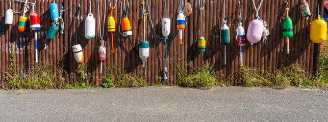 A panorama of a wooden fence decorated with old lobster floats in the village as a symbol of the...