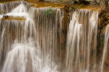 Fototapeta premium The close-up of a waterfall in layers with brown rock and trees from Thailand.