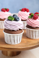 Wooden dessert stand with sweet cupcakes on light table, closeup