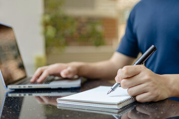 Online studying concept the man who is working from home attempting to write the meeting report down while online meeting of his company is conducting