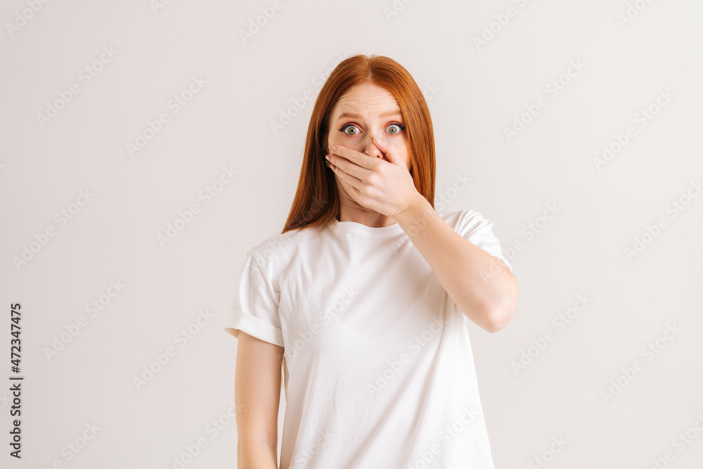 Wall mural studio portrait of astonished shocked young woman covering mouth with pressed palms popping eyes at 