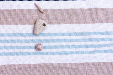 Stone with hole, snail shell, sea shell on striped beach towel. marine items