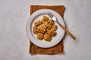 Homemade Italian gnocchi from whole grain flour, baked pumpkin puree and parmesan on light plate with fork and napkin on concrete background. Top view