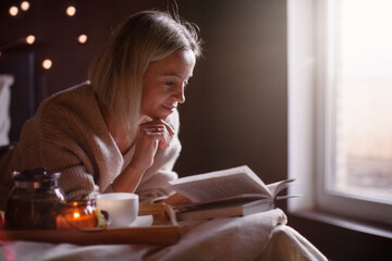 Adult 40s woman is reading a book in bed at cozy home