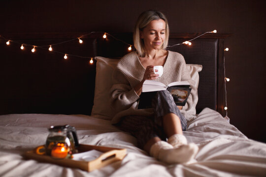 Adult 40s woman is reading a book in bed at cozy home