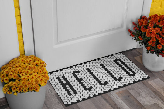 Stylish door mat with word Hello and beautiful flowers on wooden floor