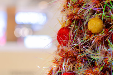 Red and gold baubles hanging on colorful Christmas tree with blurred background with space for text.