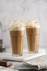 Two tall glasses with cold coffee drink frappe - iced cappuccino with whipped cream on a marble...