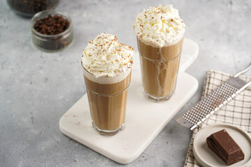 Two tall glasses with cold coffee drink frappe - iced cappuccino with whipped cream on a marble...