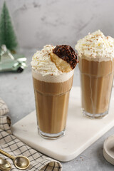 Two tall glasses with cold coffee drink frappe - iced cappuccino with whipped cream on a marble board and christmas ornaments and decoration