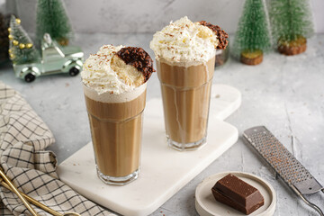 Two tall glasses with cold coffee drink frappe - iced cappuccino with whipped cream on a marble board and christmas ornaments and decoration