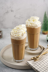 Two tall glasses with cold coffee drink frappe - iced cappuccino with whipped cream, christmas decoration and trees