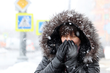 Cold weather and blizzard in winter city. Woman in fur hood standing on a street during snowfall...