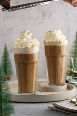 Grating chocolate over two tall glasses with cold coffee drink frappe - iced cappuccino with...