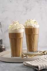 Two tall glasses with cold coffee drink frappe - iced cappuccino with whipped cream on a concrete tray