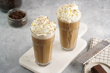 Two tall glasses with cold coffee drink frappe - iced cappuccino with whipped cream on a marble...