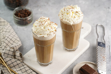 Two tall glasses with cold coffee drink frappe - iced cappuccino with whipped cream on a marble board