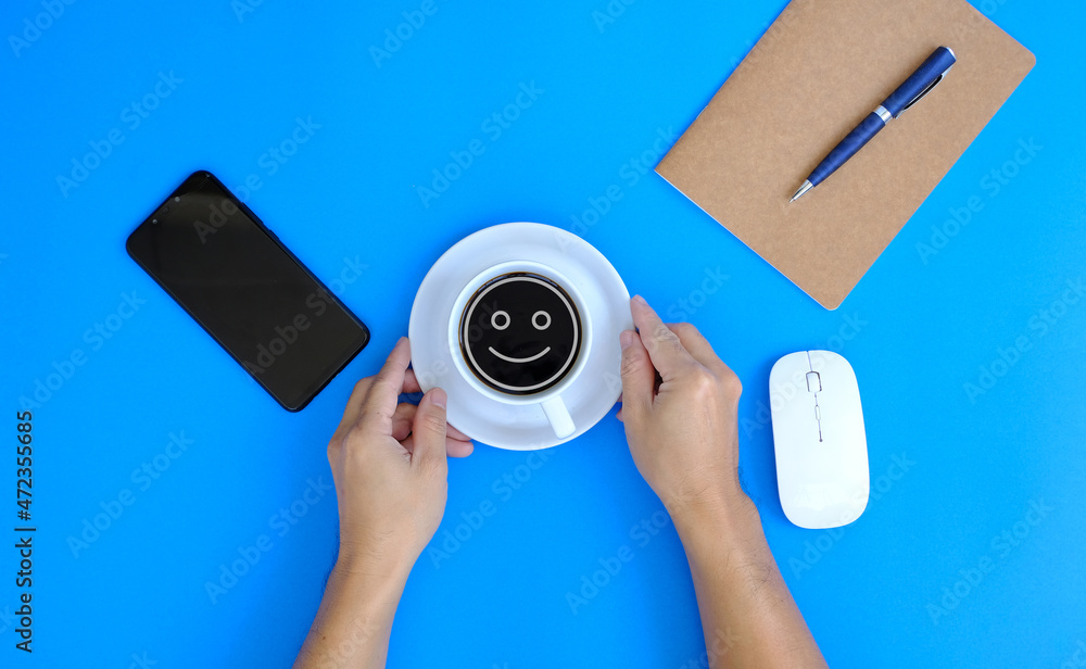 Poster person holding a coffee, office desk table with computer tools and supplies is a blank notebook with