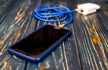 Mobile phone and charger on brown wooden background
