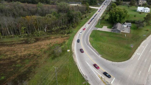 Corvette car parade through rural roads in Wisconsin. Cars turning onto highway. Residential home and garage on corner. Multiple directional signs present. 