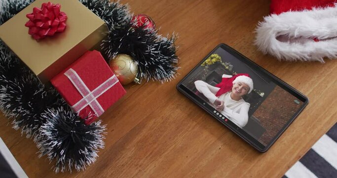 Smiling caucasian woman wearing santa hat on christmas video call on tablet